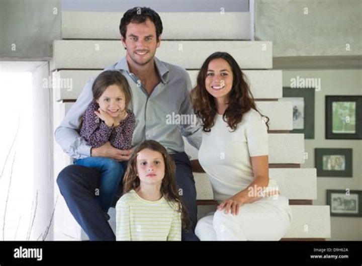 a family sitting on steps in front of some trees and bushes, posing for