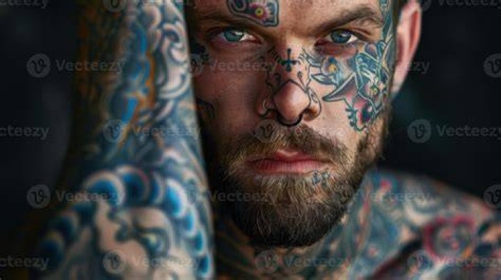 a man with tattoos on his arm holding a cell phone while standing in