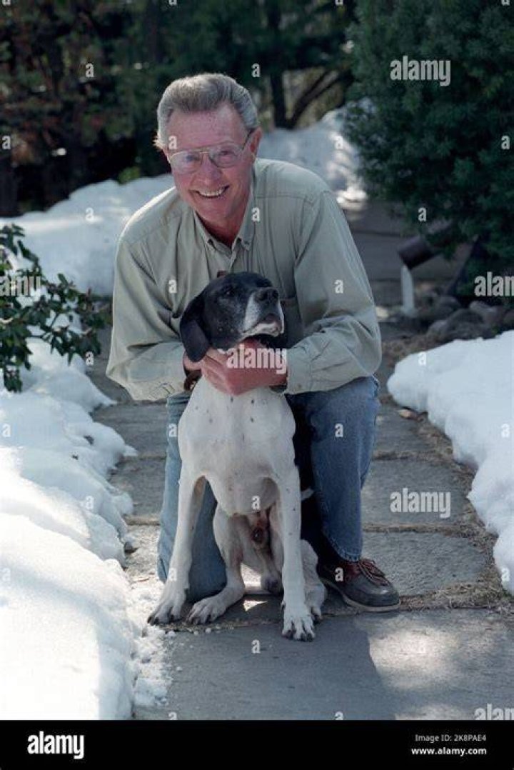 Mike Horstman with his dog Adele at his feet and bear tans in his background cabin wall.