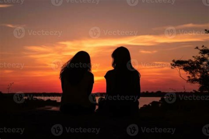 two women sitting next to each other in front of a window with the